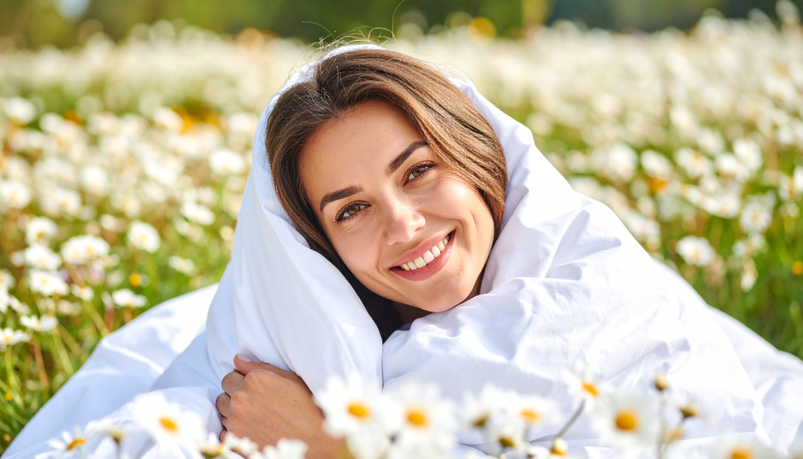 Eine Frau liegt auf einer Blumenwiese unter einer Daunendecke